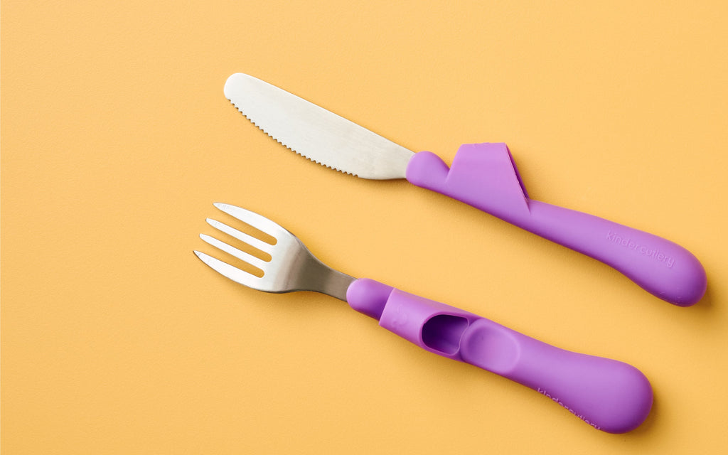 Kinder Cutlery's purple fork and knife children's training cutlery set, which helps children independently cut their own food, on a yellow background.
