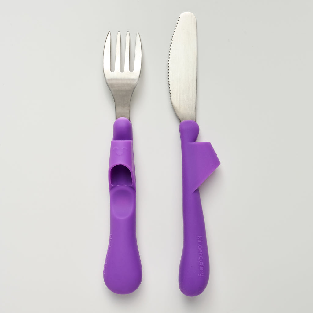 Kinder Cutlery's purple fork and knife set, made of stainless steel and food-grade silicone handles, on a light gray background